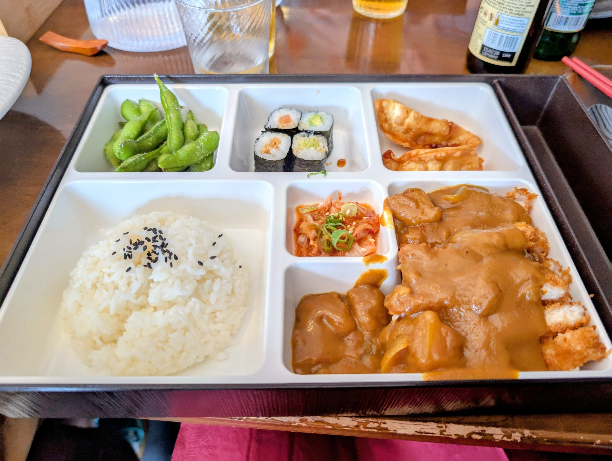 A katsu curry "Lunch Box" including sticky rice gyoza, sushi, kimchi and edamame.