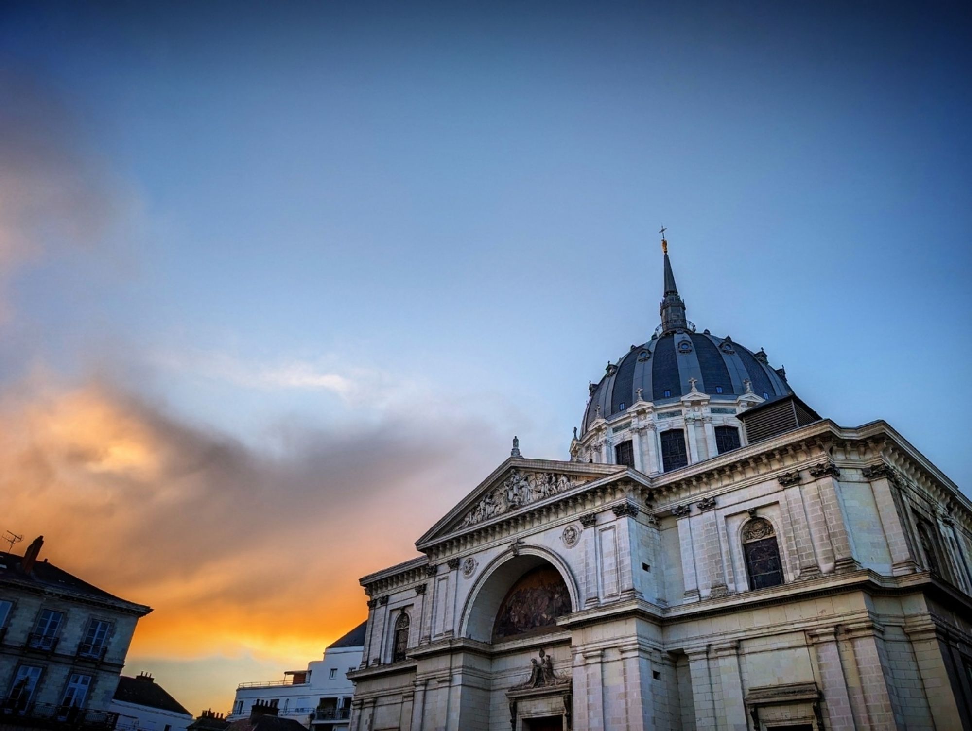 Église avec une grande coupole sur fond de coucher de soleil avec une belle lueur orange sur la gauche.