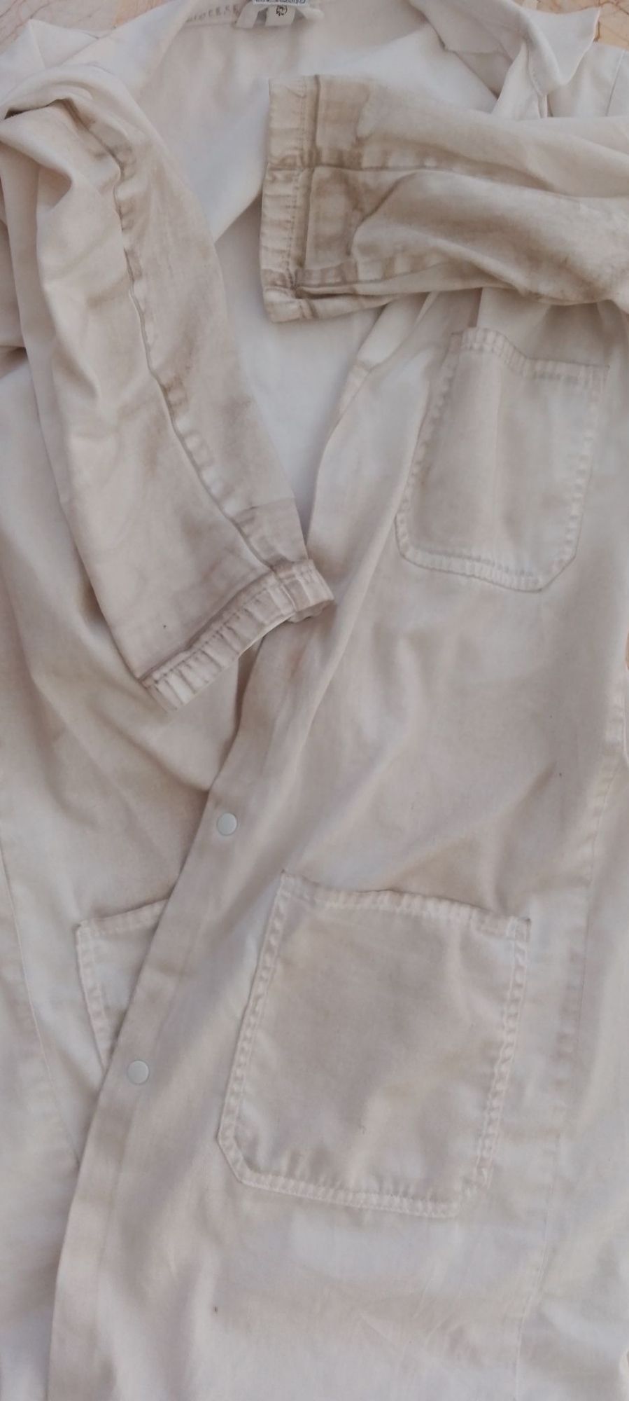 Blouse "blanche" couverte d'une couche marronnasse, voire noire, sur les manches et aux poches.