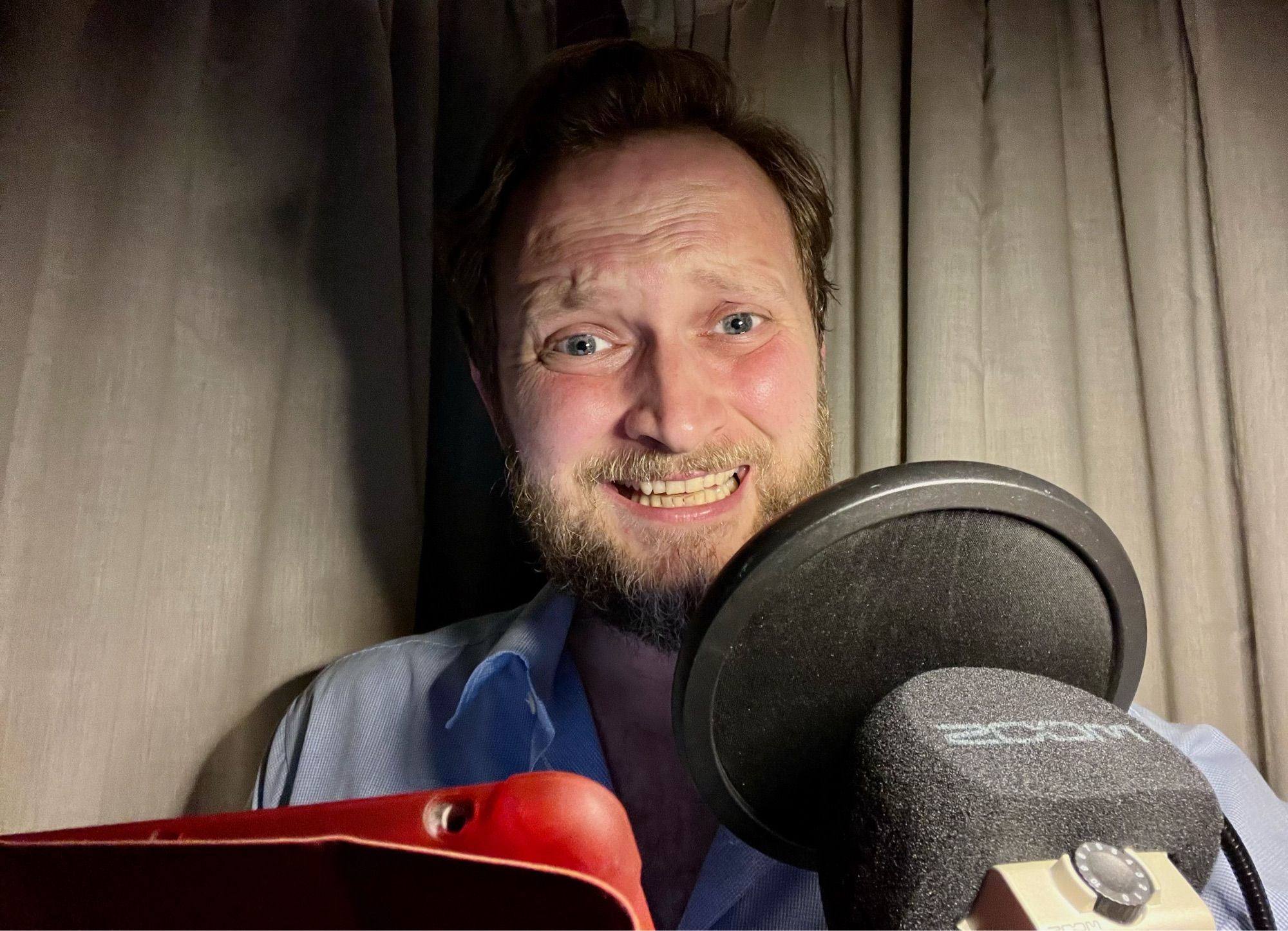 A demented Tom Crowley pictured in his home studio with a microphone and an insane grin.