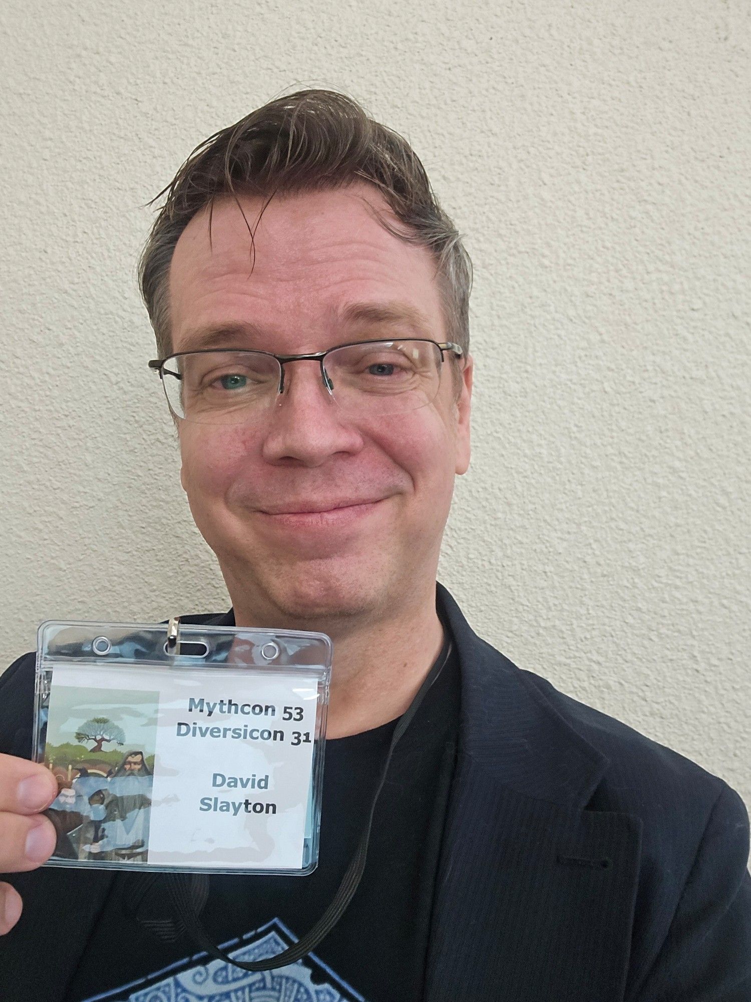 Photo of one tired David holding up his Mythcon 53 / Diversicon 31 badge.