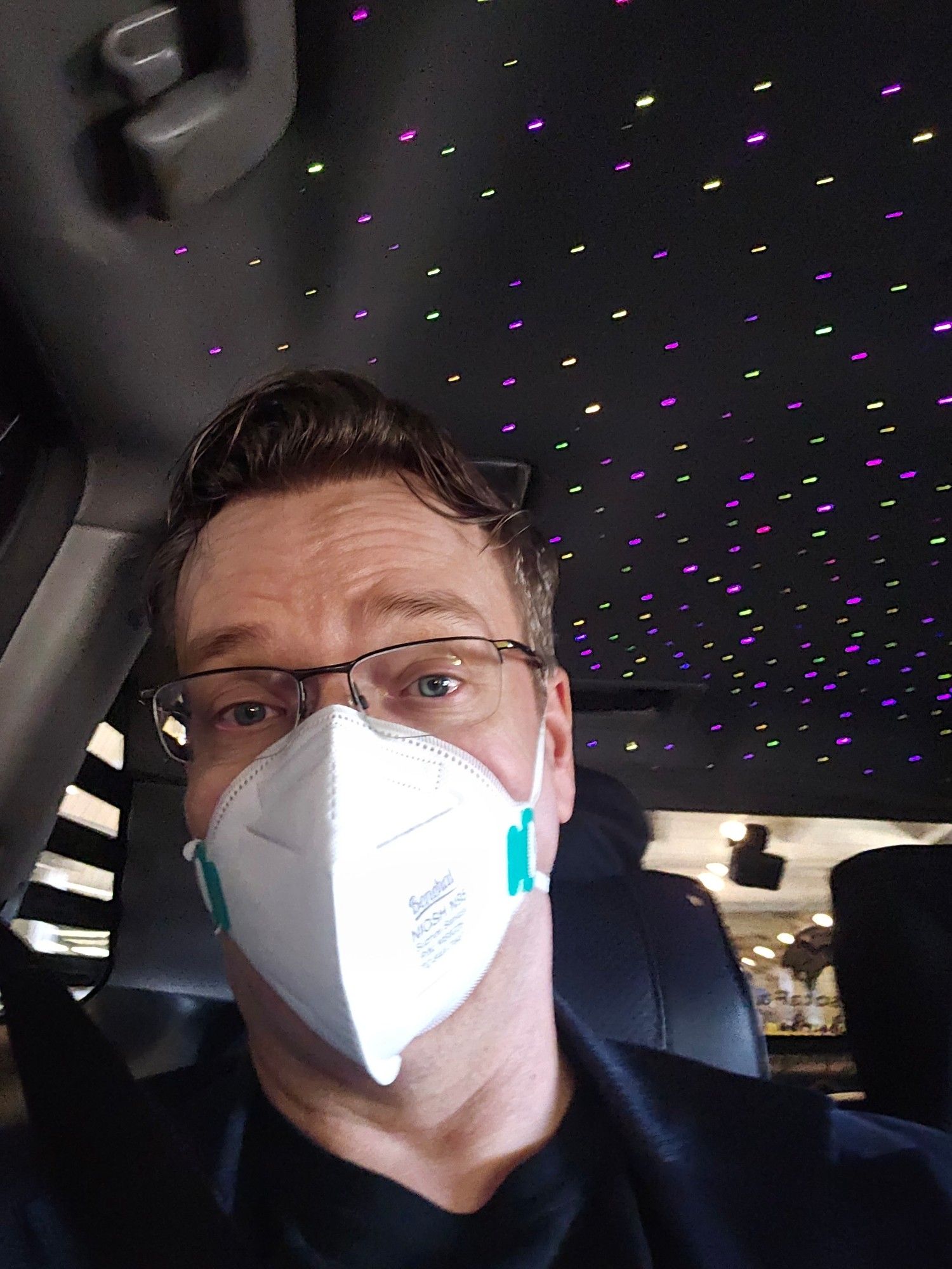 David, masked in a car with purple and green lights embedded in the ceiling.