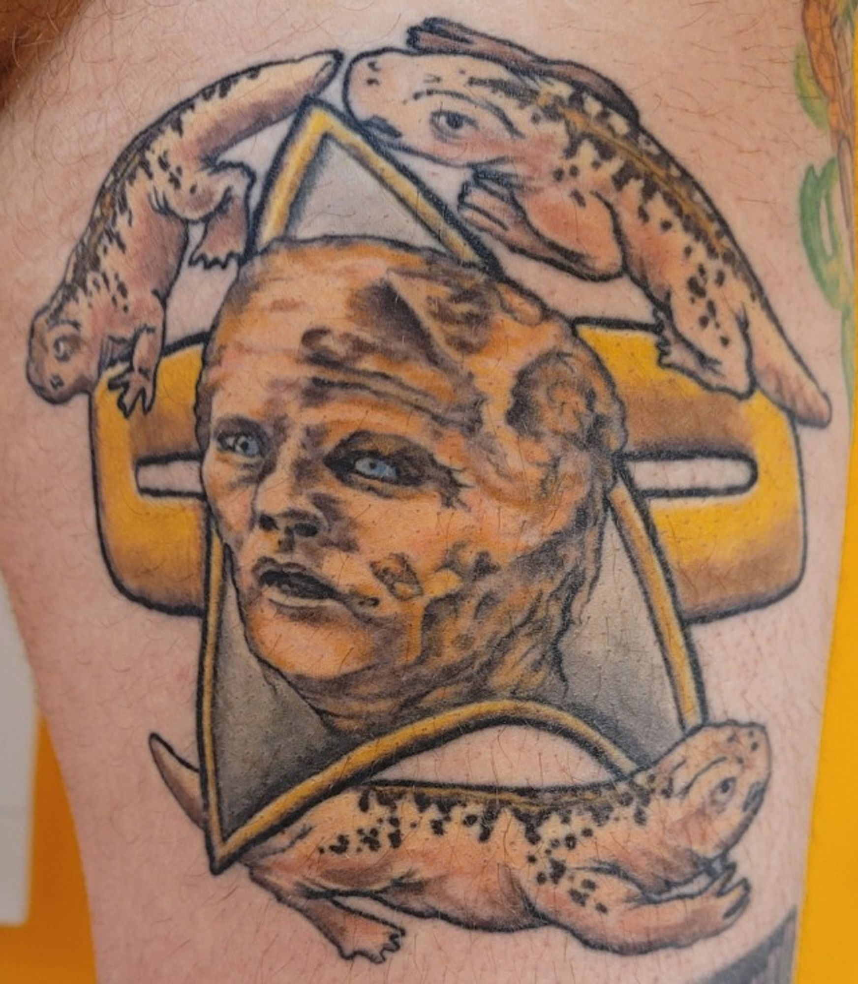 Tattoo on a man's thigh of a partially-mutated Tom Paris from Star Trek Voyager episode 2.15 "Threshold." His face is emblazoned on a Voyager-era comm badge and is surrounded by his and Janeway's three children who were cruelly abandoned by Chakotay.