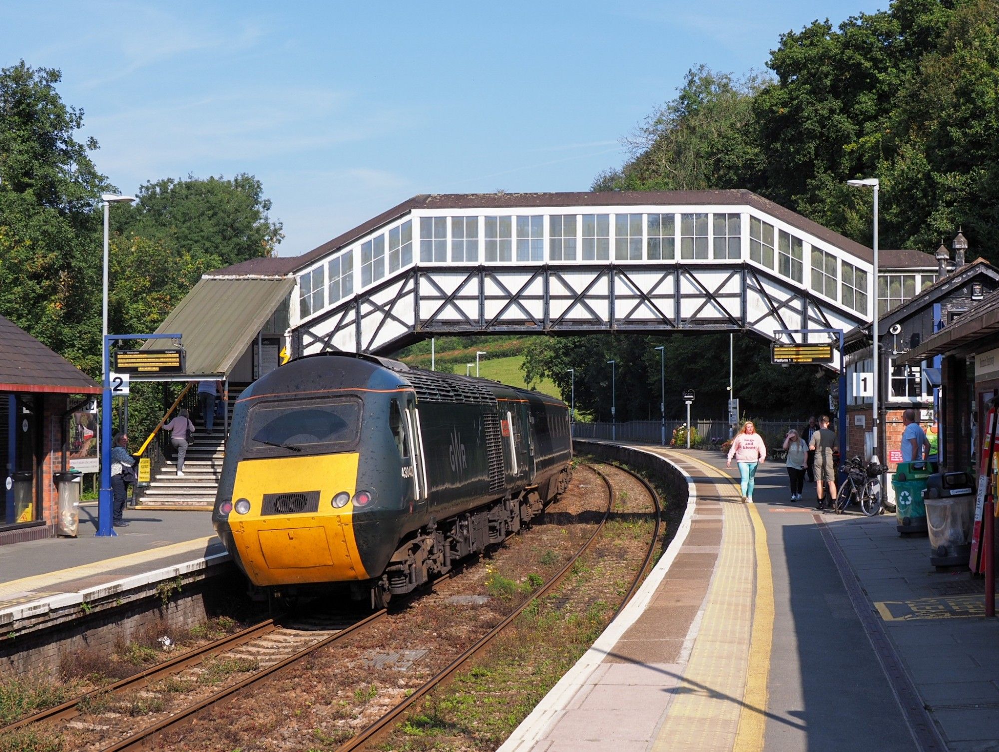 Rear power car of an HST under the old foot bridge. Lattice girder structure painted green, white wooden panels and windows behind it.