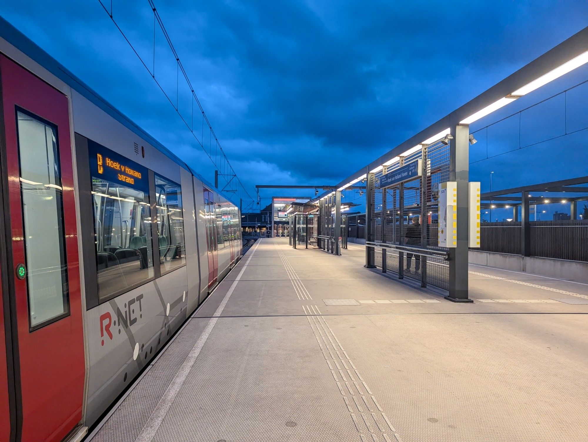 A metro train in the modern open-air station of Hoek van Holland Haven at blue hour.