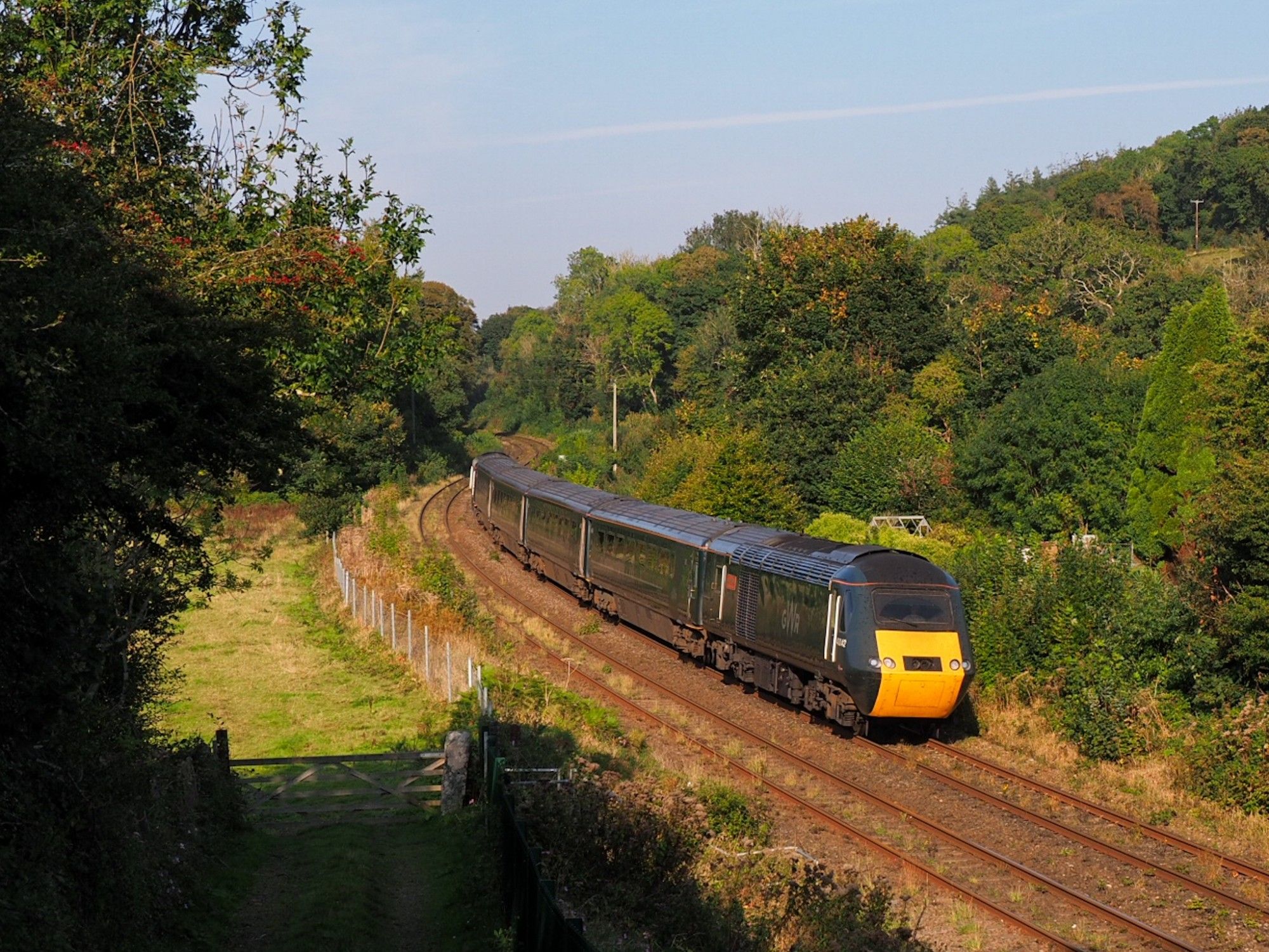 A GWR HST [for non rail people: Britains 40-years-old, legenday former diesel Intercity high speed train] also known as "Castle Sets" speeds through a curve in a very green landscape.