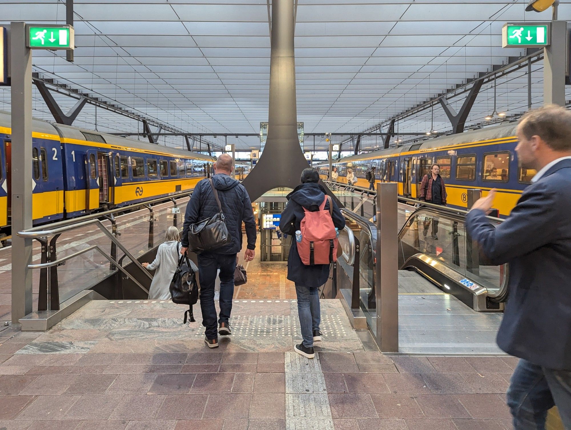 Two classic IC Internationaal trains standing side by side at Rotterdam-Centraal. People take the stairs down to the underpass in the middle