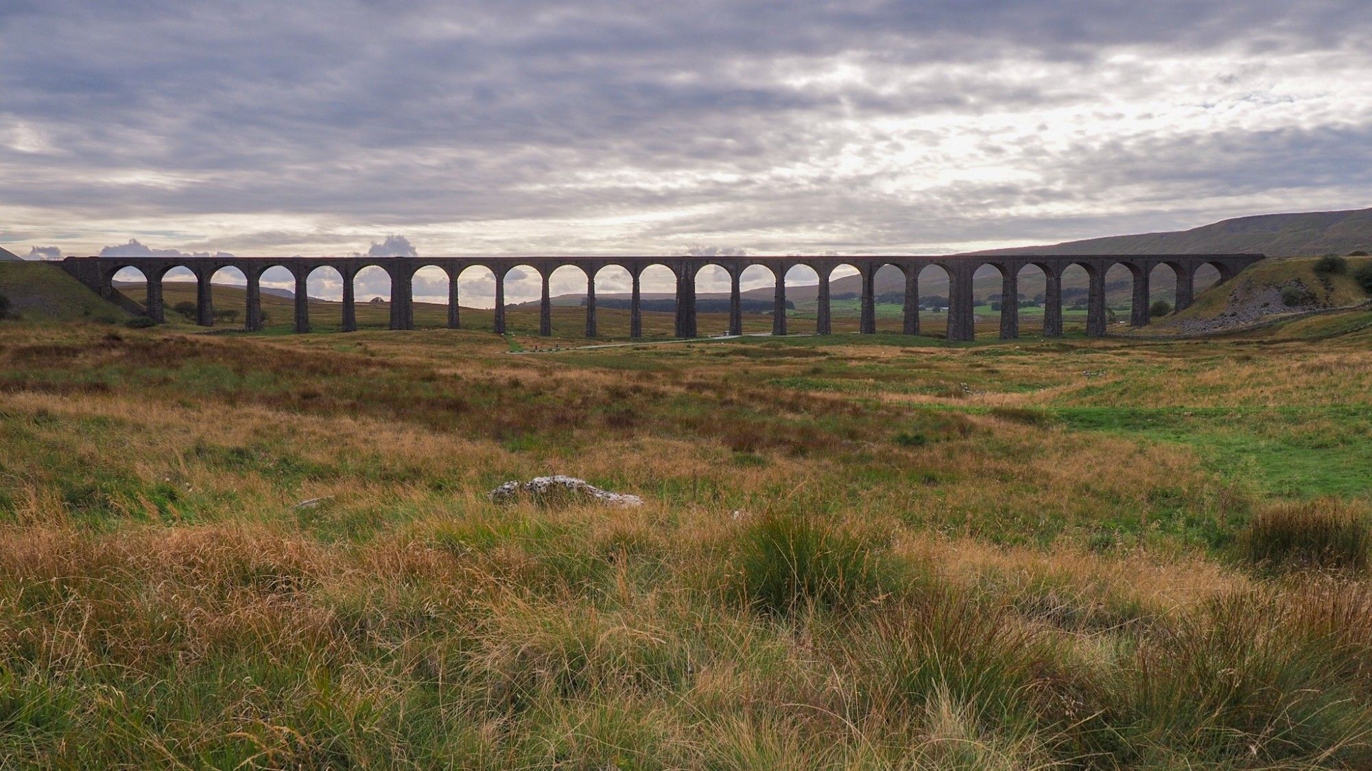 Lateral view of the viaduct against the light. Silhouette of the arches against the moor and a cloudy sky.