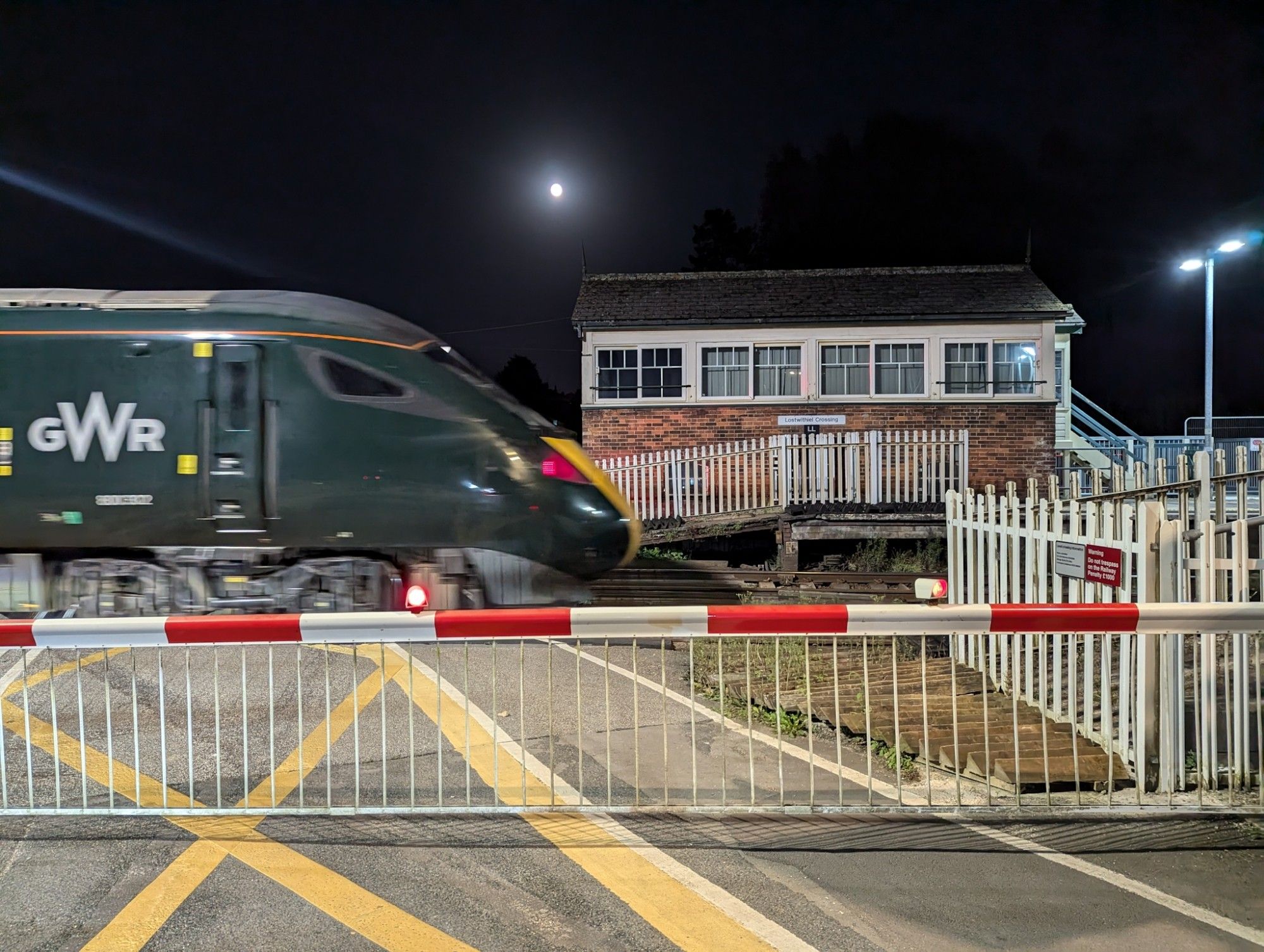 An IET train crosses Lostwithiel level crossing in front of the former signal box, the (nearly) full moon above it