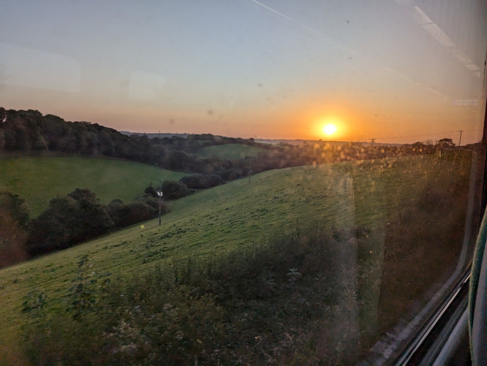 View through the train window: The sun sets behind soft green hills of Cornwall.