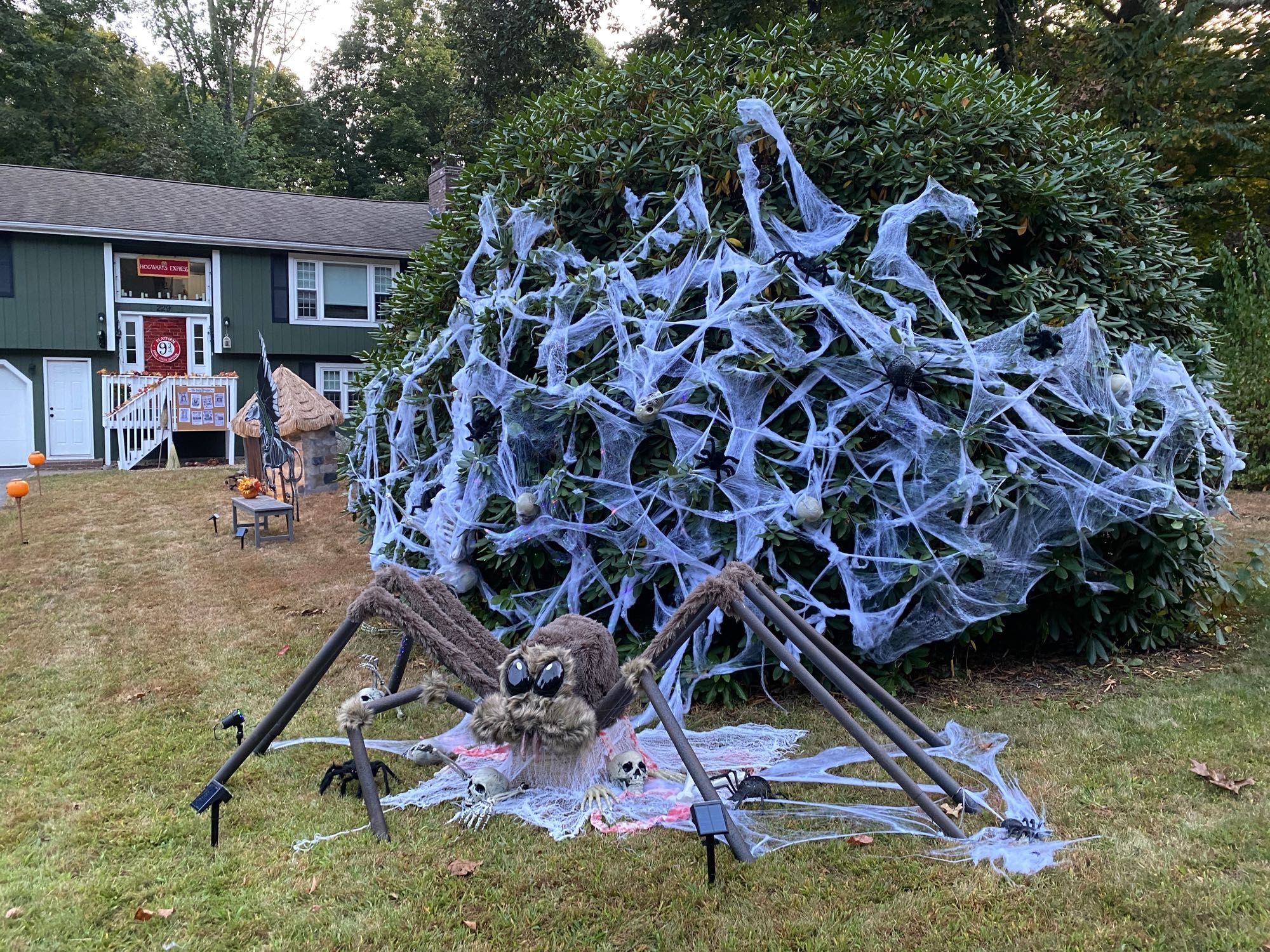 A Halloween decoration Harry Potter themed giant spider with cobwebs and skeletons and in the background is a house with a Hogwarts Express Platform 9 3/4 sign