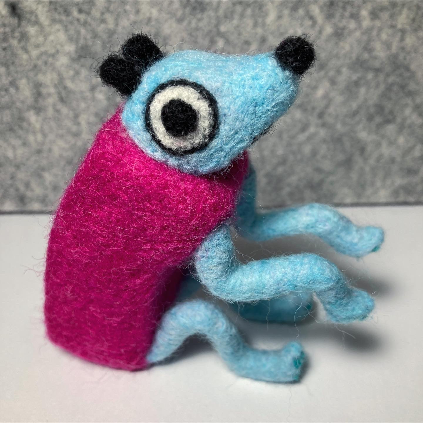 A photo of a needle felted Wobbledog from the game Wobbledogs. It's posed to sit on it's hind legs with it's front legs in the air.