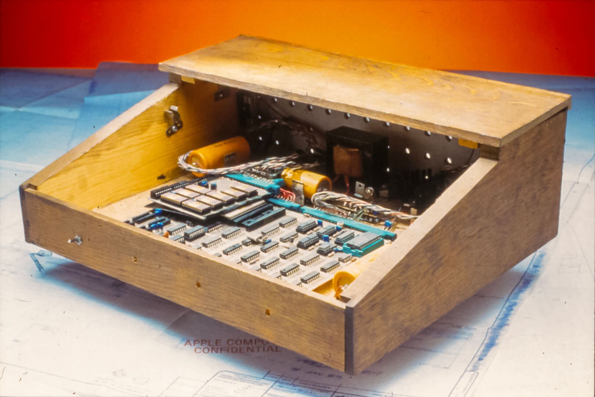 The prototype used to develop the Apple 1.  The wooden case is adapted from a breadbox (the holes for mounting on a wall and some of the hardware for the sliding cover is still visible), the wiring is hand-soldered, giant Sprague capacitators like yellow soda cans are along the back, and the chips are hand-placed in a grid.