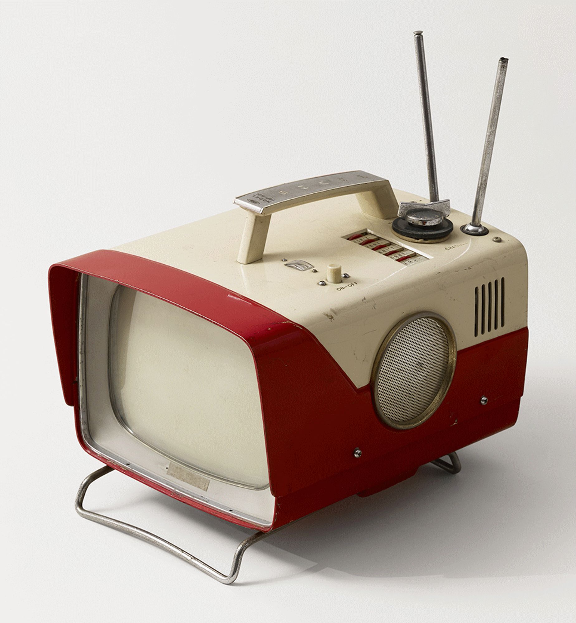 A portable television, in a very 'space age' case:  the top is ivory but the sides and frontispiece are cherry red.  Twin antenna sprout from the back, a silver tilted carry handle sprouts from the top, and a huge silver grille allows both airflow and speaker.  There are a bare minimum of controls on the top of the device itself:  an on/off push toggle, a silver tuning dial, a rotary display behind a glass window for current station, and recessed plastic wheels for h-hold, v-hold, brightness, and volume.