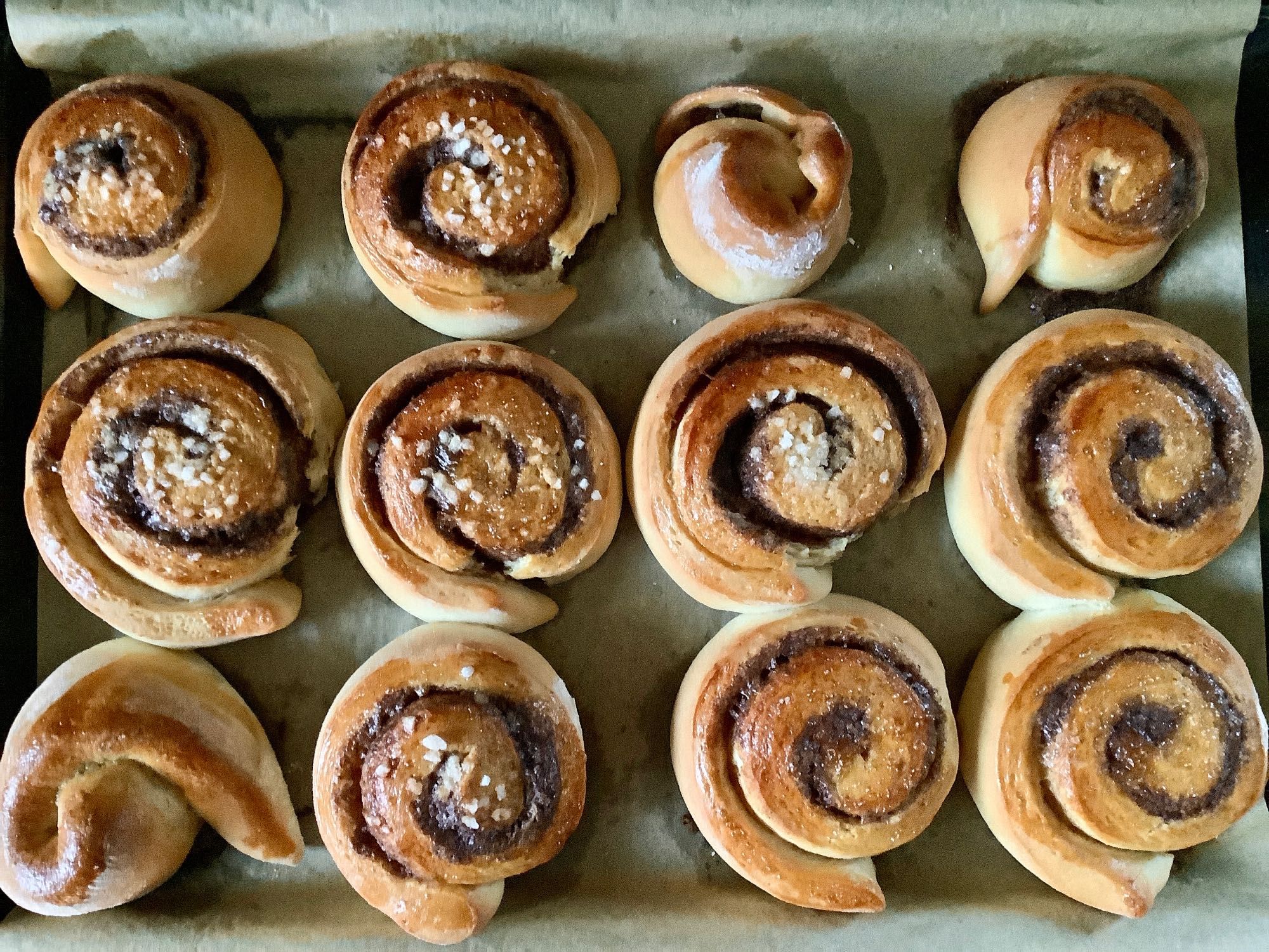 Ein Blech mit 12 duftenden Zimtschnecken von oben fotografiert. Ein paar sind mit Hagelzucker dekoriert.