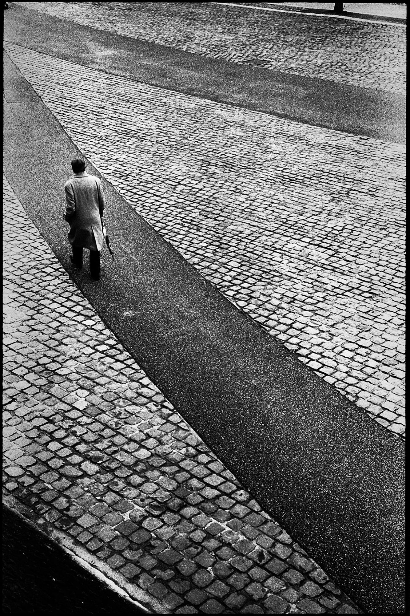 A black and white film photography of an elegant man walking in the street, with a graphical composition.