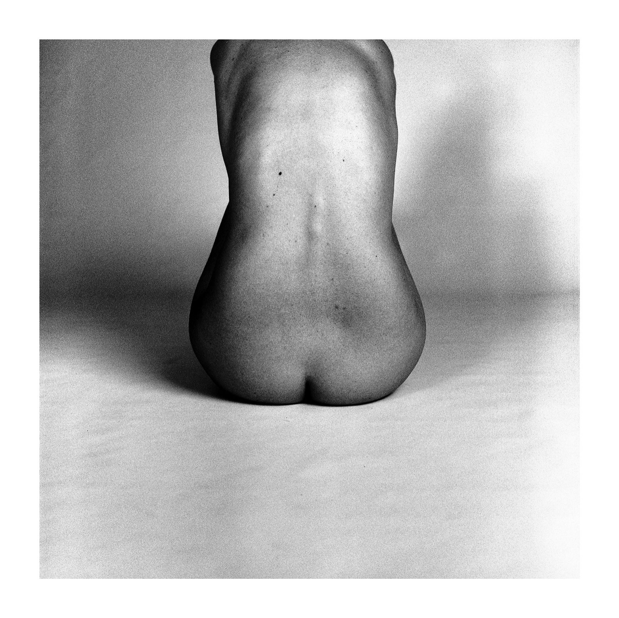 Black and white analog photograph of a sitting nude woman's back.