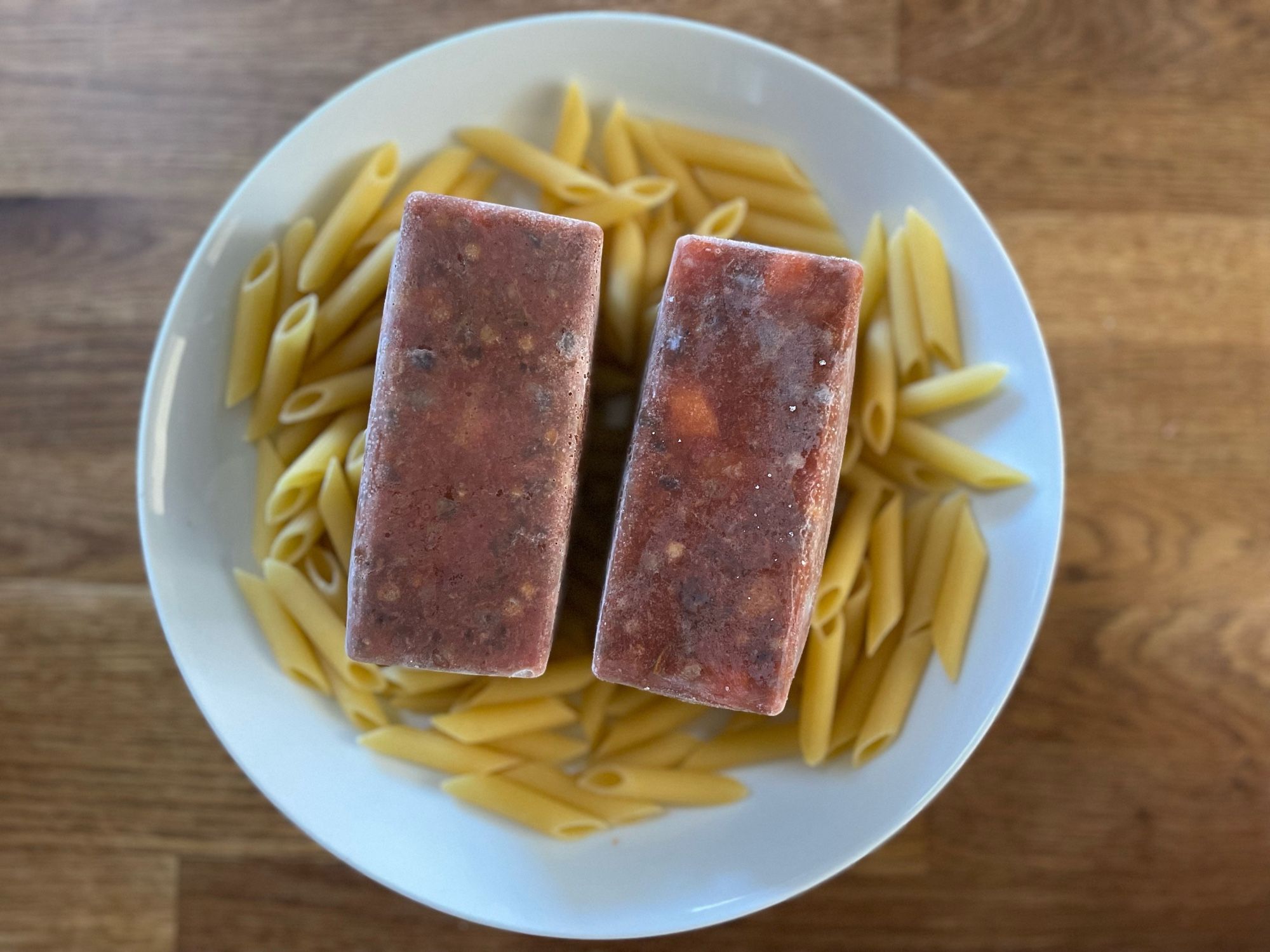 Frozen ragu ice cubes on penne pasta in bowl