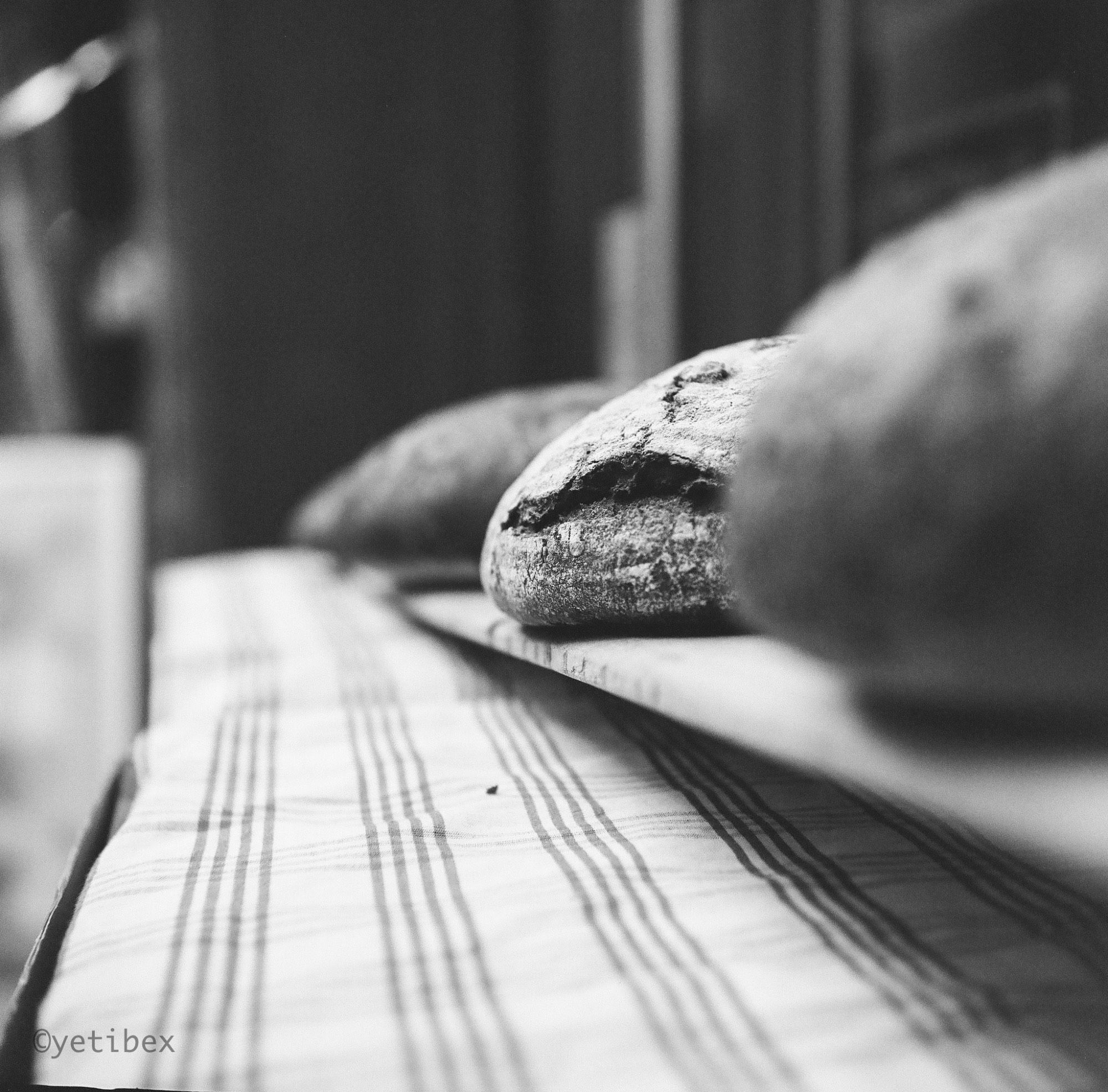 A black and white image of three loaves of bread. Only the middle loaf is in focus.