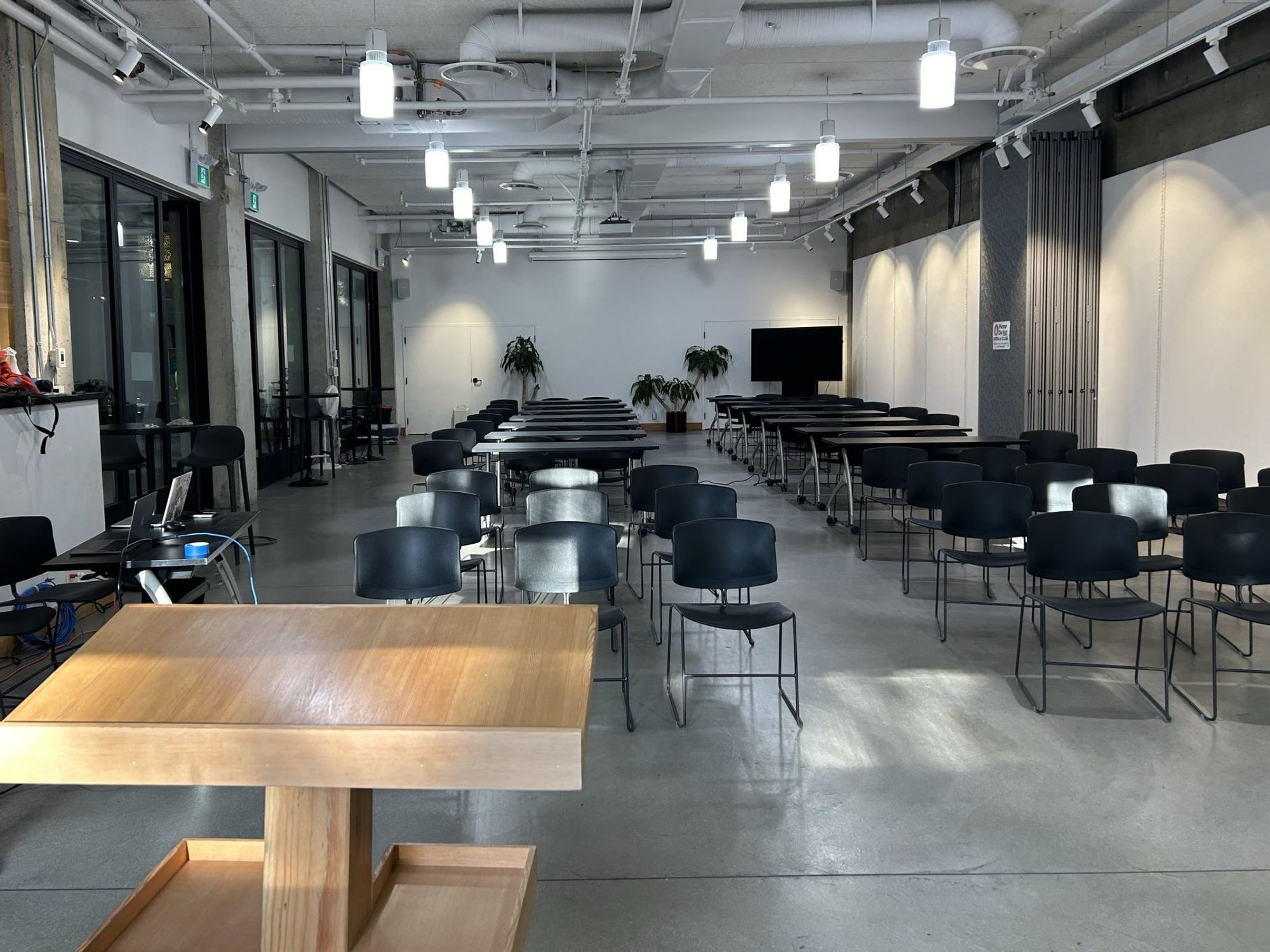 Room with a wooden podium in the foreground looking out at black chairs and black and grey tables.