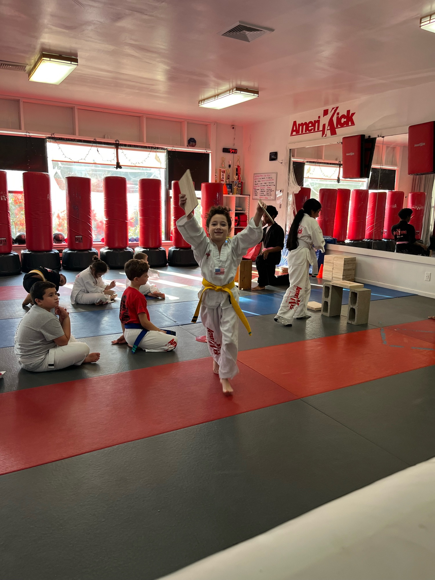 Child in karate uniform with yellow belt holds up pieces of broken wooden board 