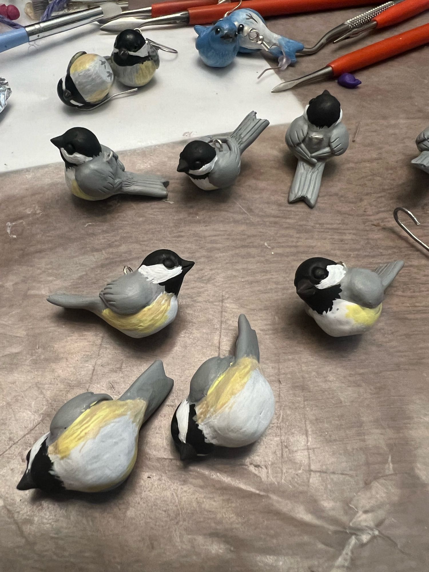 Tiny unfinished polymer clay chickadees are scattered across a sheet of wax paper.