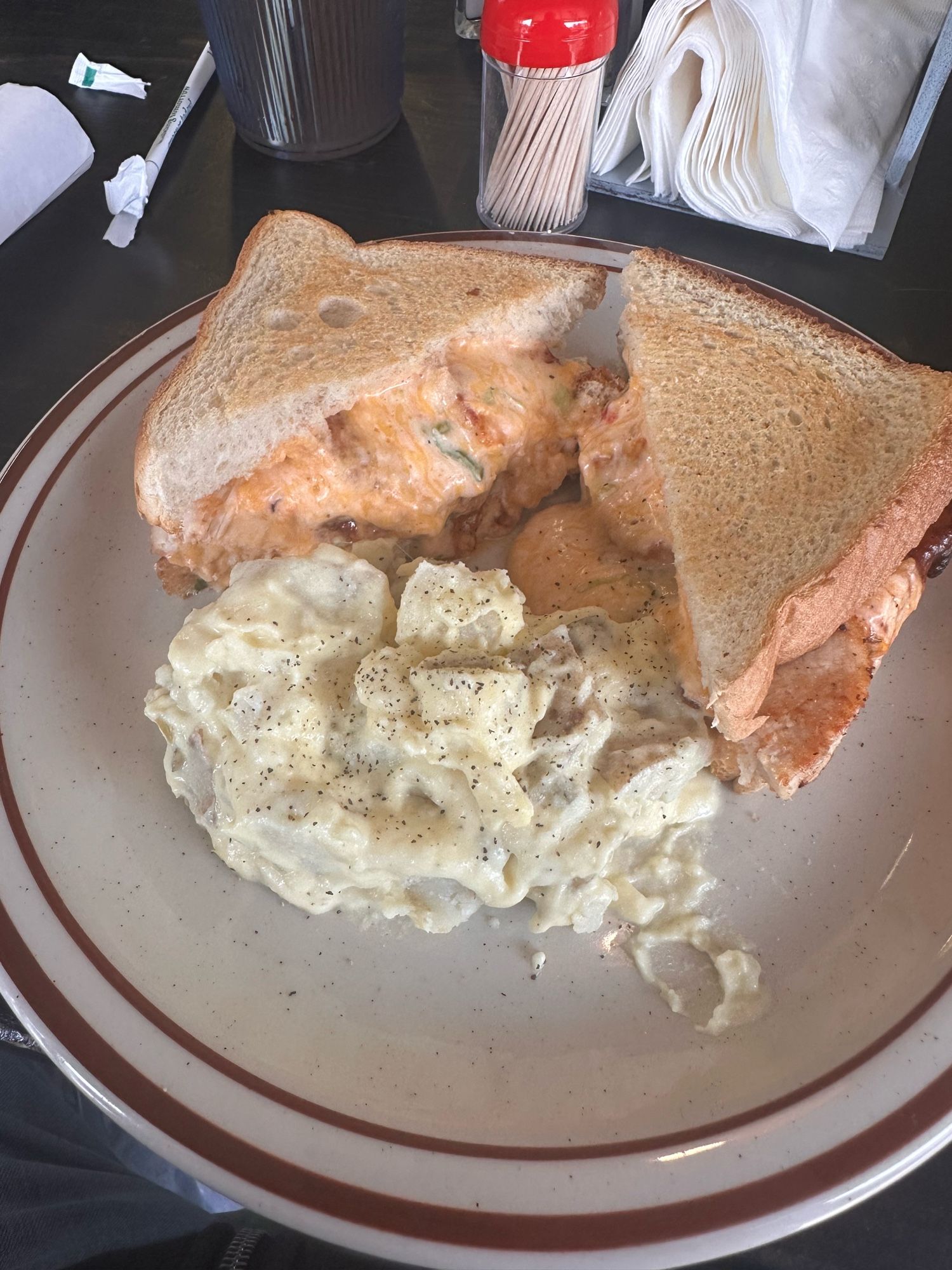 A sandwich with chicken drenched in pimento cheese with potato salad on the side