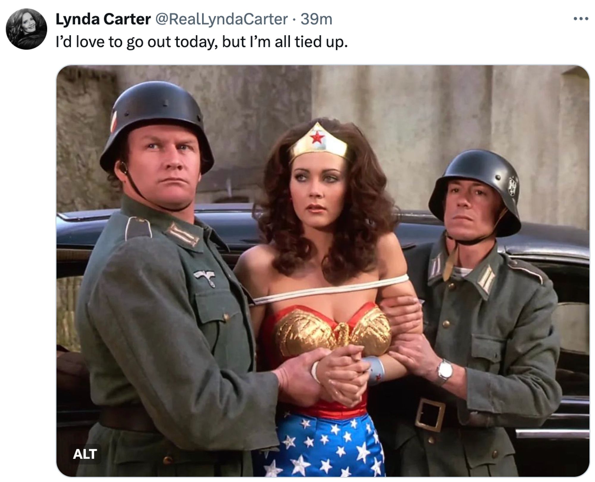 Screenshot of a social post by Lynda Carter ('@RealLyndaCarter' on the social platform 'X') that says: 'I'd love to go out today, but I'm all tied up.' Attached is a photo of Lynda Carter under arrest as Wonder Woman.