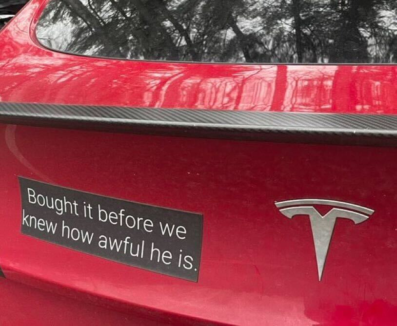 A photo of a Tesla with a bumper sticker that reads “Bought it before we knew how awful he is.”