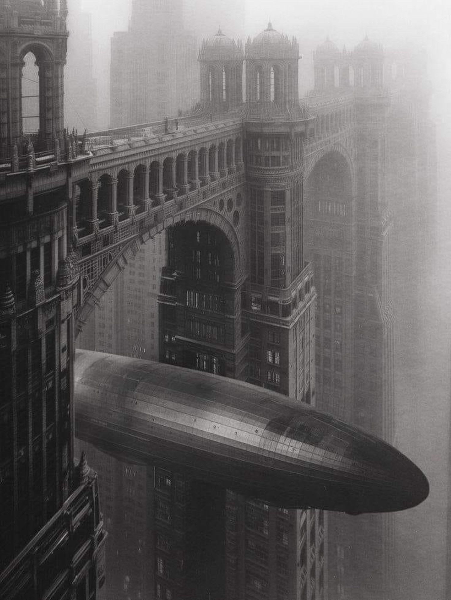 A black-and-white image depicts a large zeppelin navigating through a narrow space between two grandiose, gothic-style skyscrapers connected by ornate skybridges. The foggy atmosphere adds a sense of mystery and a bygone era to the scene.