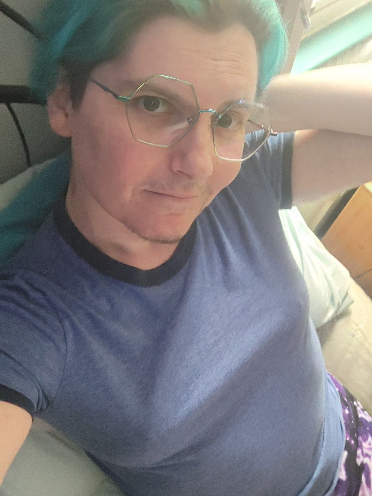 kay, a white genderfluid person, sitting on a bed.