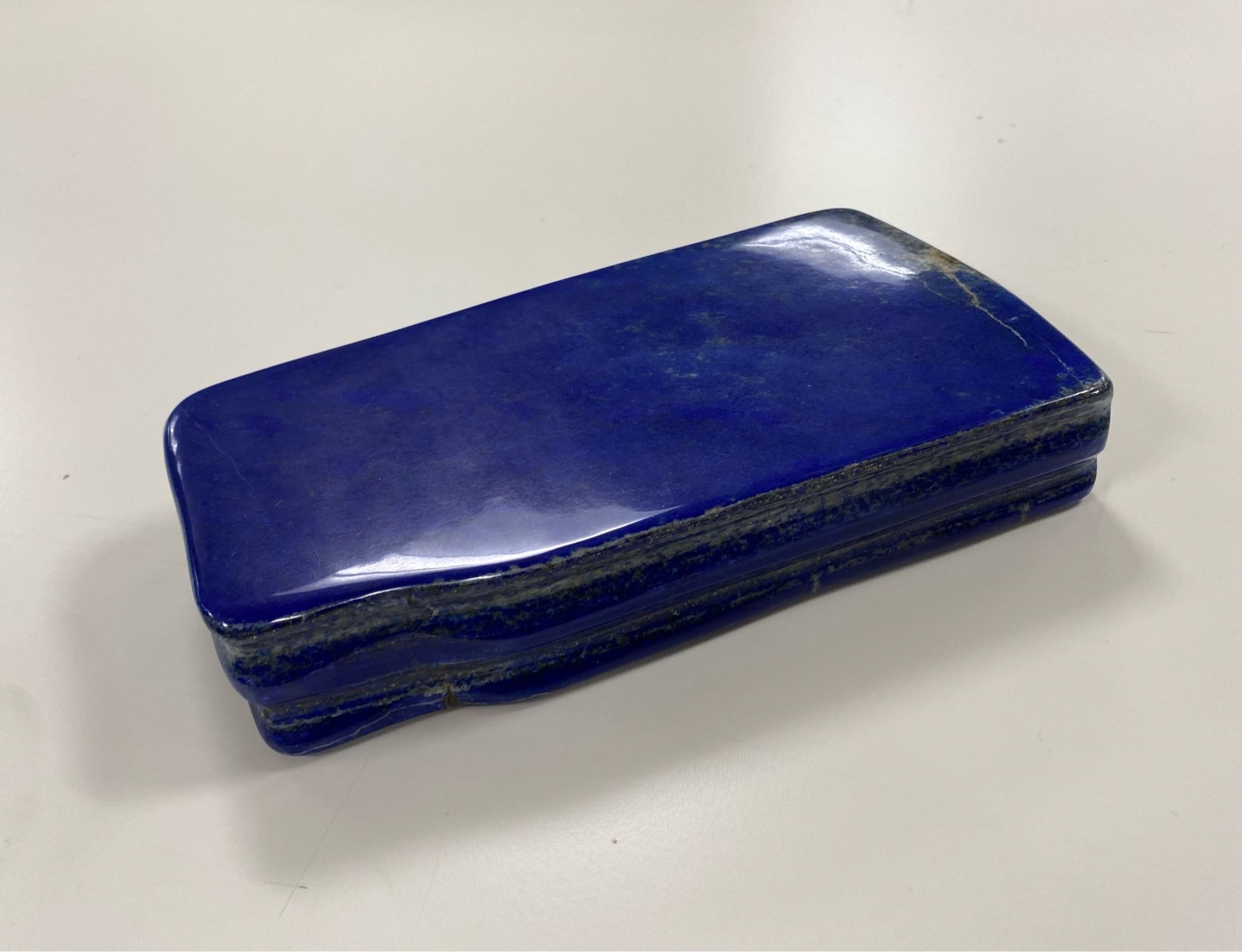 Rectangular blue lapis lazuli with a high polish specimen on a white background. The sides show 5 alternating layers of blue and grey, with the blue layers protruding a bit more. At the Hunterian.