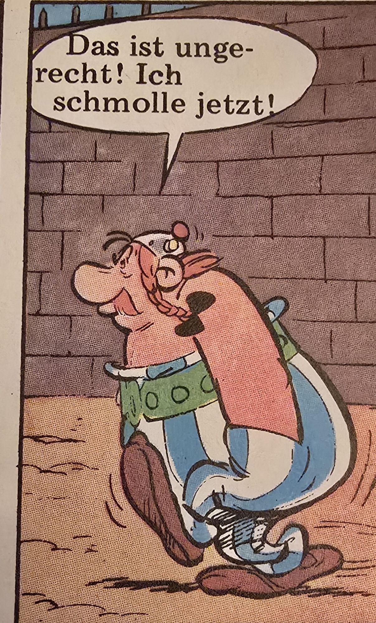 Obelix stapft mit Händen in den Taschen davon und missmutigem Gesichtsausdruck davon.
Sprechblase: Das ist ungerecht! Ich schmolle jetzt!
Szene aus Asterix als Gladiator