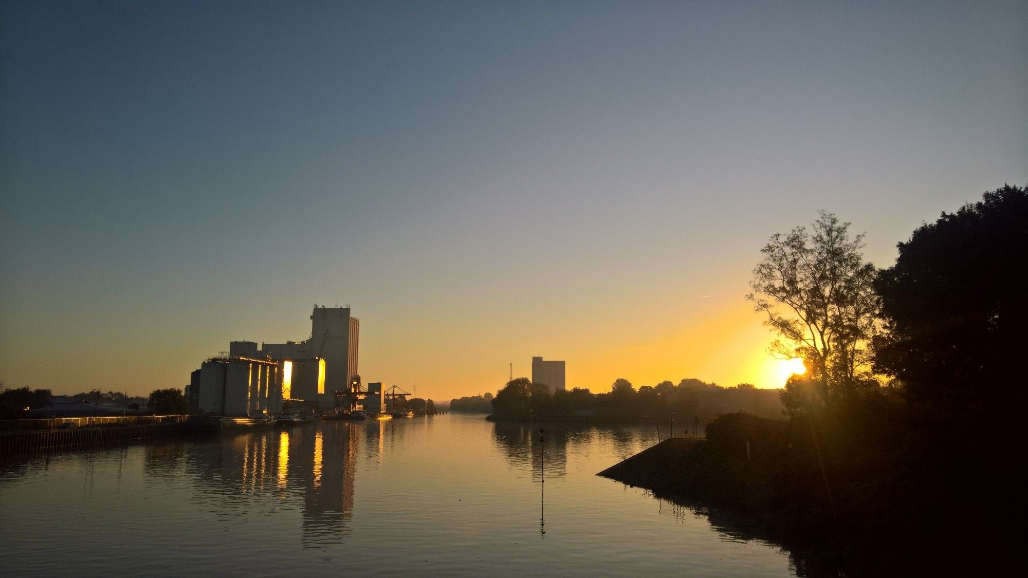 Blank geputzter Morgenhimmel über der Hunte, an deren Ufern Gebäude zu sehen sind.