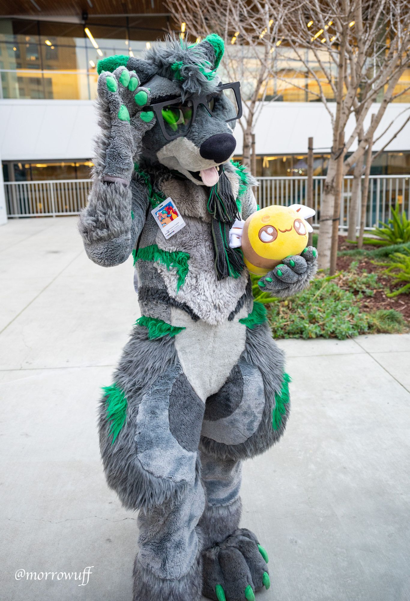 San Jose Convention Center, exterior. Photo of Bandit Raccoon (gray and green raccoon fursuiter) standing and adjusting his fursuit glasses