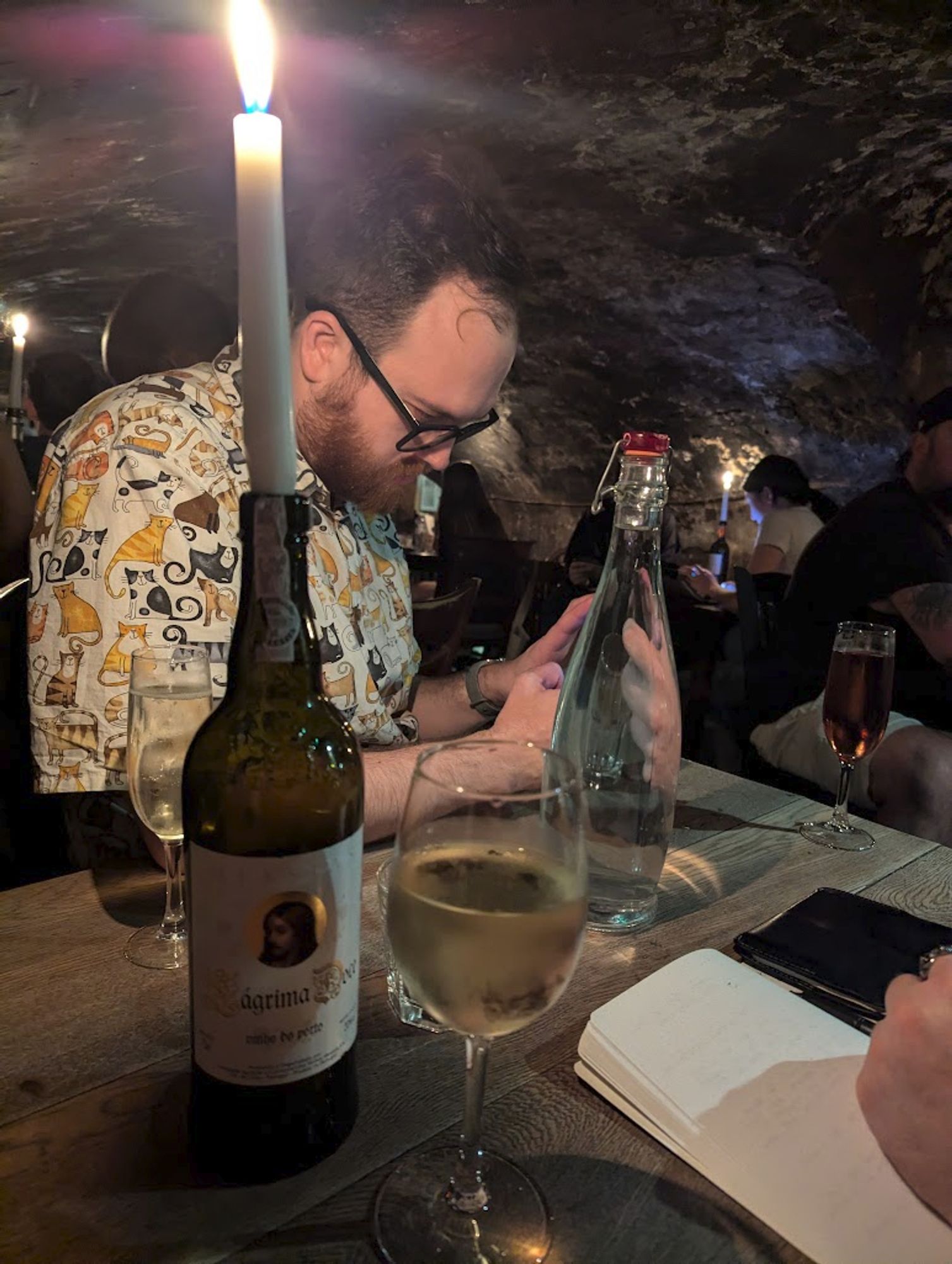 Dave taking a photo of a glass of wine in an underground, candlelit wine bar