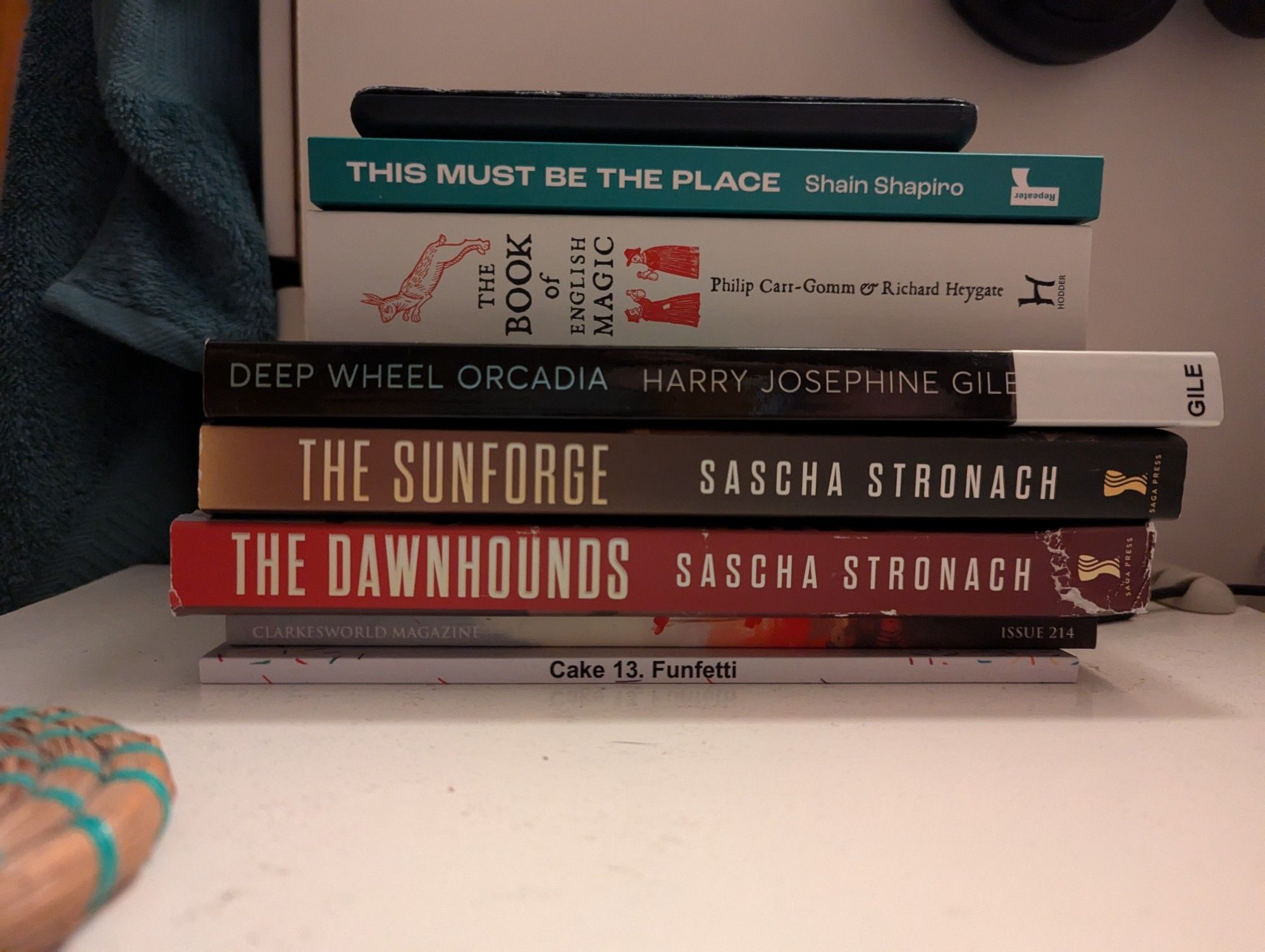 A stack of books - This Must Be the Place by Shain Shapiro, The Book of English Magic by Philip Carr-Gomm & Richard Heygate, Deep Wheel Orcadia by Harry Josephine Giles, and The Dawnhounds and The Sunforge, both by Sascha Stronach