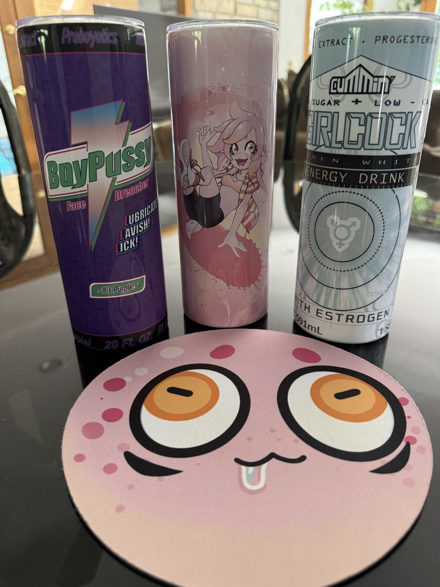 From Left to Right, A Parody Gatorade Drink Tumbler, called "BoyPussy" The Face Drencher, With ProBOYotics, Lubricate, Lavish, Lick. Its Purple Flavor, The middle Tumbler is a pink Squid person sliding across some ink, the 3rd Tumbler is A Parody Gridlock Energy Drink Tumbler called "Girlcock" Semenwhite Energy Drink with Estrogen. 
in front of and between all of them is a circular PORB Mousepad.