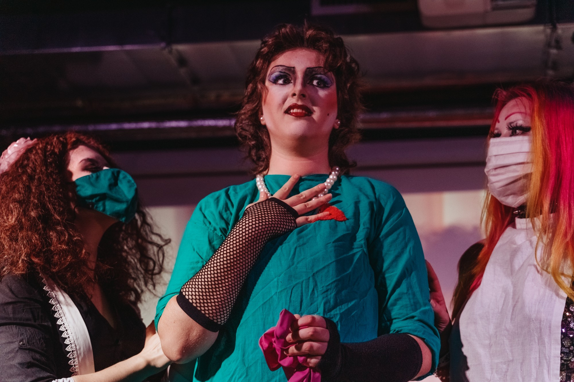 Jay as Frank'n'Furter in the laboratory scene looking to the right, hand on his chest, surrounded by Magenta on the left and Columbia on the right 