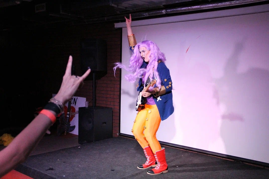 Jay as Akira Otoishi on stage rocking out with his electric guitar, his hand and an audience member's hend on the left signing "yeeeaahh roockkk"