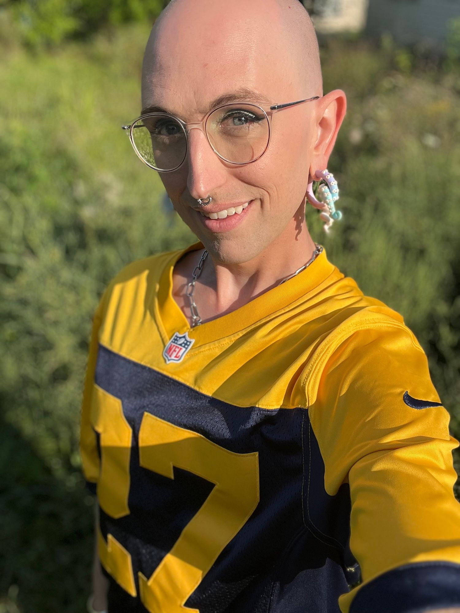 A bald femme person in a too-large Packers throwback jersey