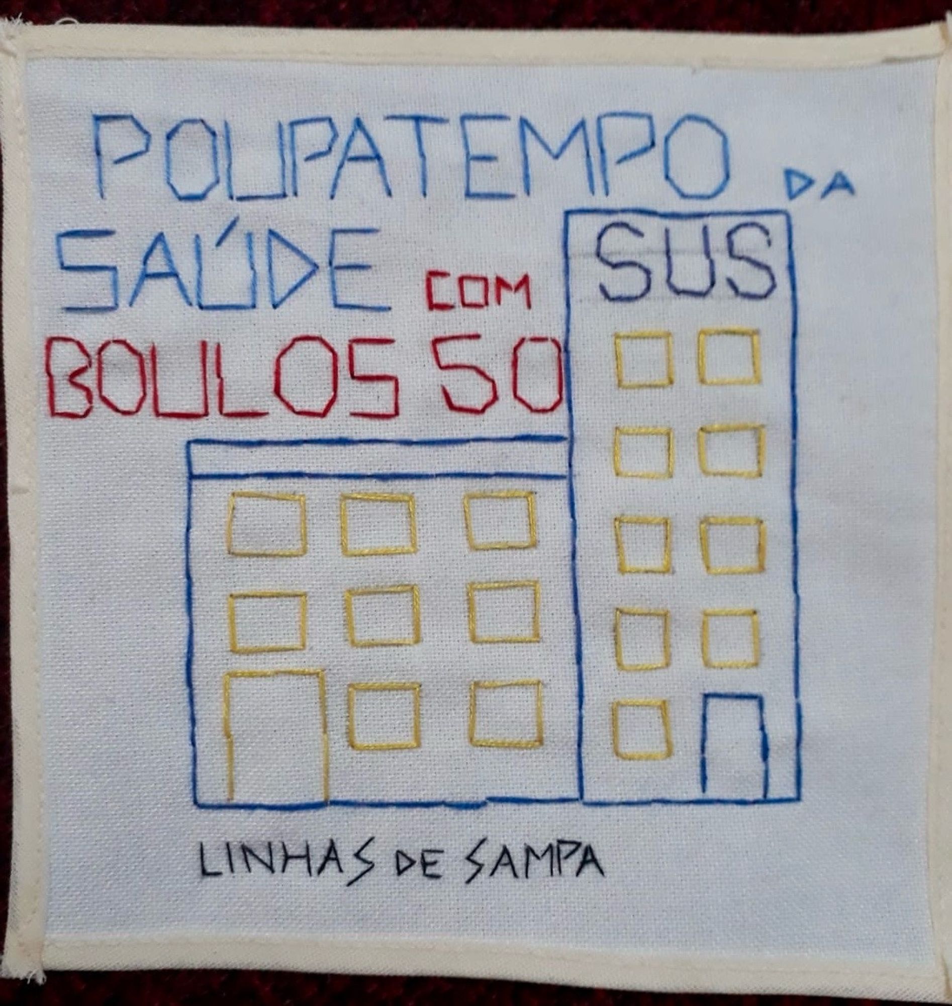 Bordado sobre quadrado de tecido claro com desenho de um prédio com a sigla SUS no alto e os dizeres “Poupatempo da Saúde com Boulos 50. Embaixo, a assinatura Linhas de Sampa