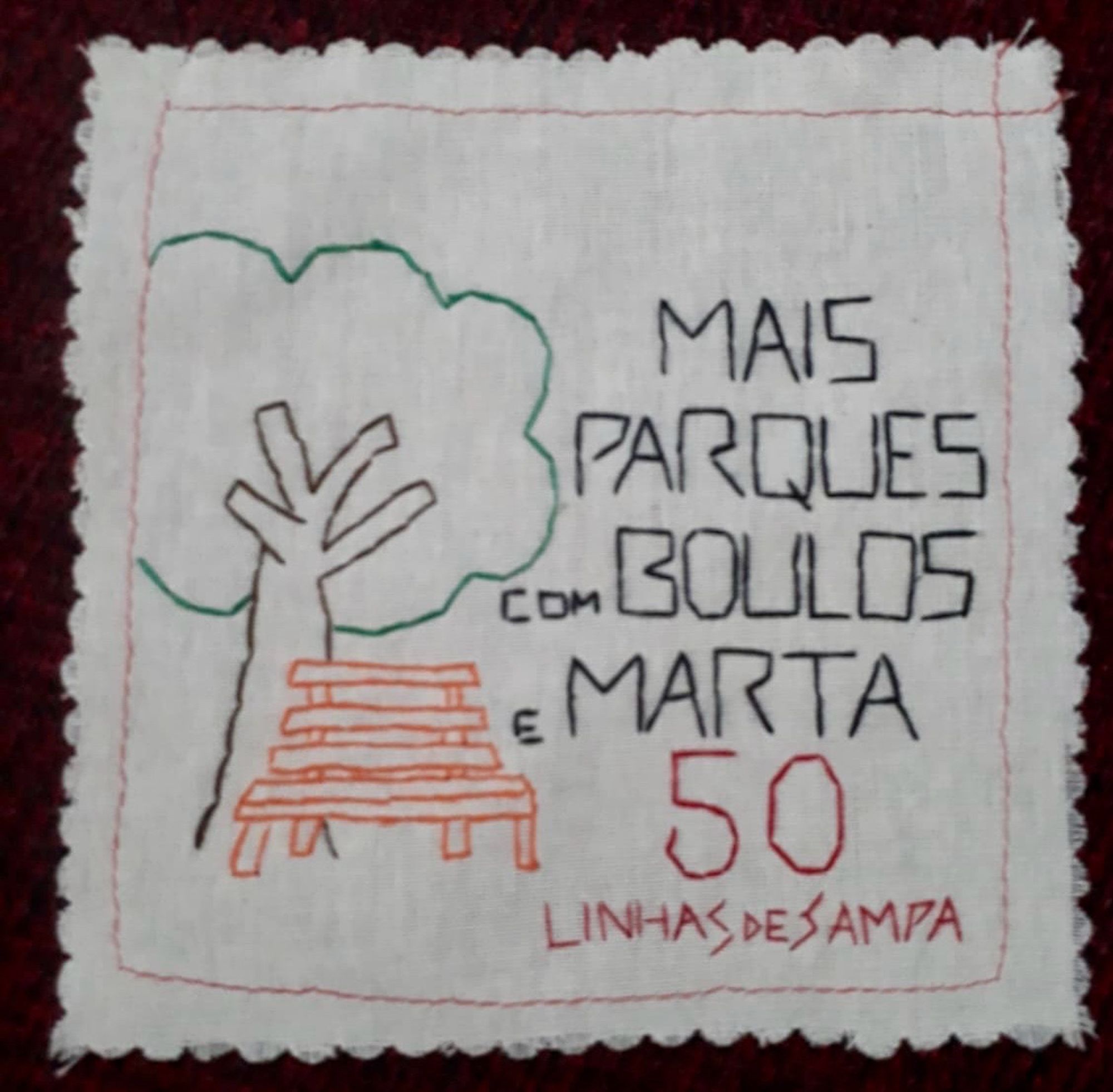 Bordado sobre quadrado de tecido claro com desenho de uma árvore e os dizeres “Mais parques com Boulos e Marta”, seguidos do número 50. Embaixo, a assinatura Linhas de Tampa