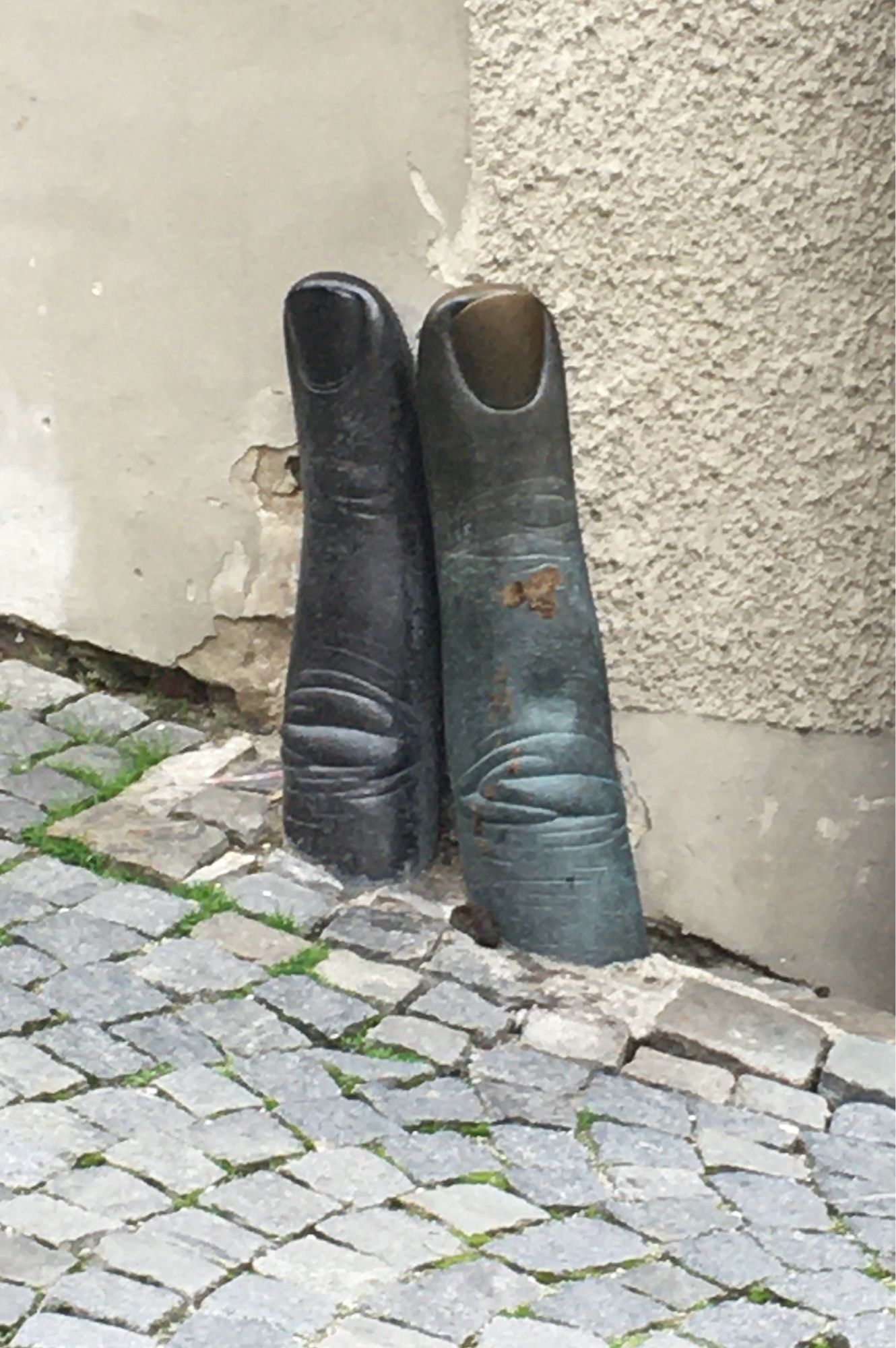 2 Finger Skulpturen aus Bronze ragen aus dem Kopfsteinpflaster ganz knapp an der Hauswand.