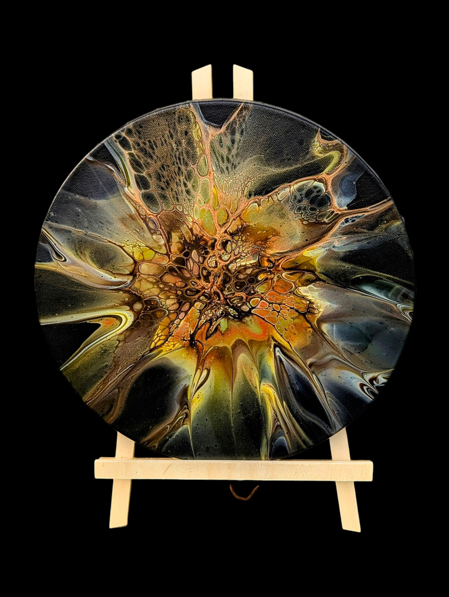 A fluid art bloom displayed on a wooden easel over a black background; the background of the painting itself is also black, the main colors are primarily shades of yellow along with a hint of deep orange and olive green, and the cell activators are Van Dyke brown and old gold.