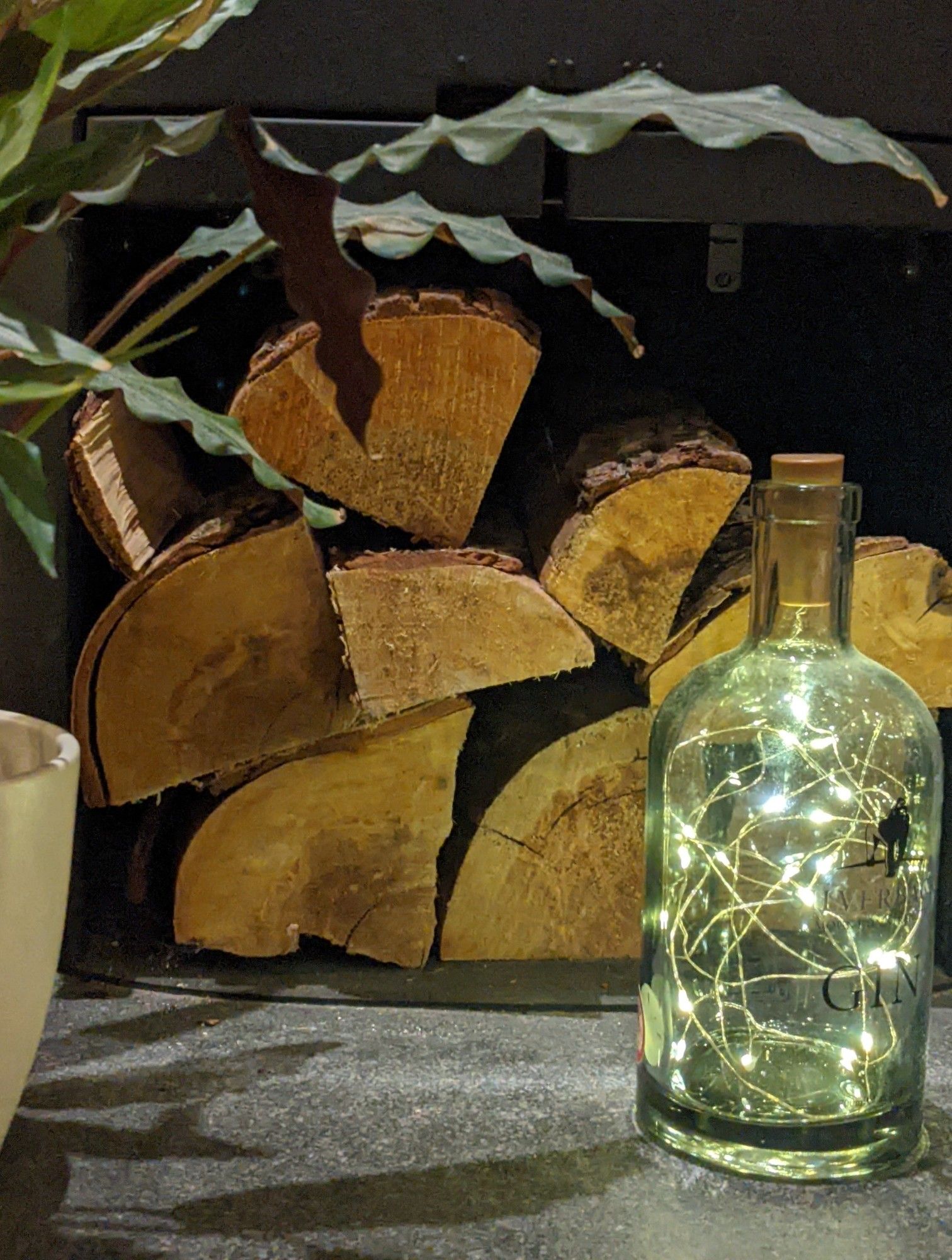 Logs ready in the under wood burner log store and a gin bottle filled with fairy lights.