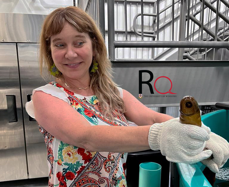 Dr. Sara Good stands over water tank with gloves holding a lamprey, a large eel-like fish with circular teeth. Photo supplied by Sara Good.