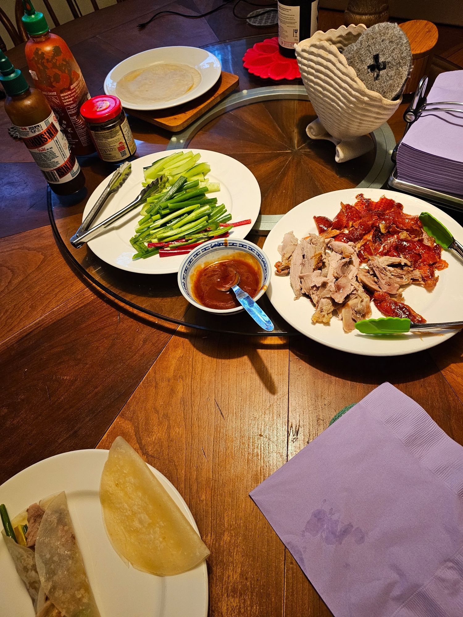 A round dining table with all the makings of Peking duck upon it.