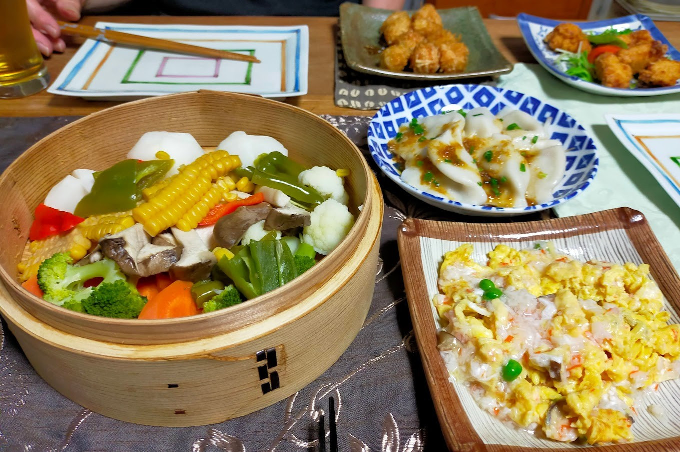 Vegetables in a steamer, kanitama, gyoza and other Chinese foods. The vegetables include corn, broccoli, cauliflower, carrots, turnips, eringi mushrooms, green and red peppers, manganji peppers, and shishito.