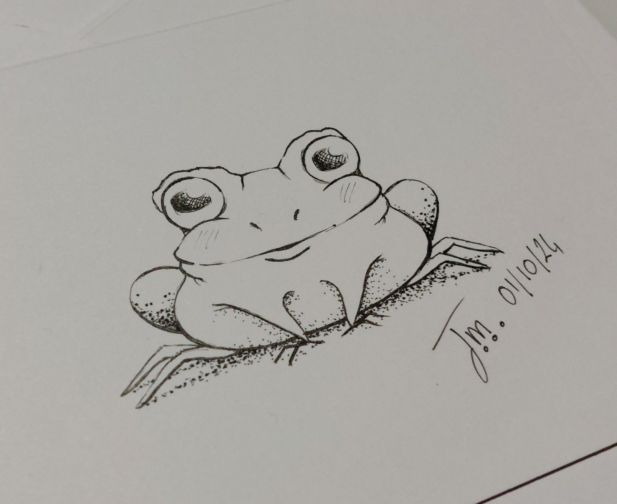 Petit dessin au feutre noir. C'est une grenouille avec de toutes petites pattes avant et de très grands yeux. La signature est composé des lettre J et M et de ma date 01/10/24.